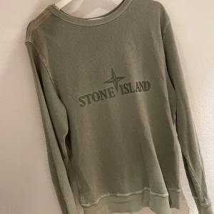 Grön tröja från Stone Island - Säljer en snygg limited edition grön tröja från Stone Island. Den har en klassisk rund hals och långa ärmar. Funkar att variera mellan bak märket som fram och fram som bak vilket är extra schysst! Perfekt för en avslappnad stil och passar bra till både jeans och chinos. Tröjan är i bra skick! 