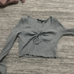 Grå ribbad croppad topp från Shein - Säljer en superfin grå ribbad topp från Shein i storlek XS. Den är croppad med långa ärmar och har en söt knytning framtill. Perfekt för både vardag och fest! 🩶