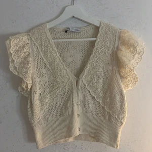Beige spetskofta från Zara - Säljer en superfin beige spetskofta från Zara. Den har korta ärmar med volangdetaljer och knappar framtill. Använt en gång och inga defekter 💕