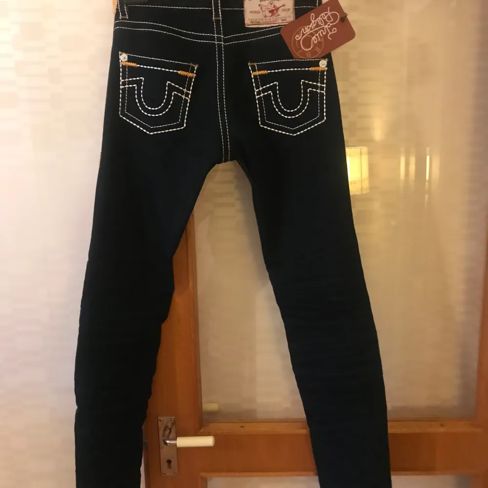 Snygga svarta jeans från True Religion med vita kontrastsömmar och coola detaljer på bakfickorna. De har en tight passform och är perfekta för både vardag och fest. Jeansen är i nytt skick och har en klassisk design som aldrig går ur stil.. Jeans & Byxor.