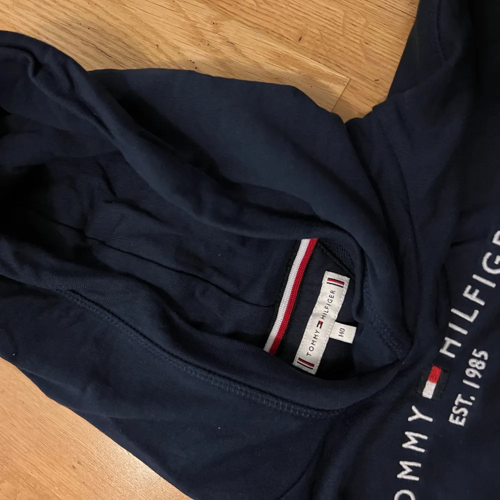 Säljer en snygg marinblå hoodie från Tommy Hilfiger i storlek 140 (barnstorlek). Den har en klassisk design med loggan tryckt på framsidan och en bekväm huva. Perfekt för både vardag och chill. Passar bra till jeans eller joggers! Nypris 695kr. Använd ett fåtal gånger. Inga fläckar eller skador. Pris går att diskuteras! . Neuletakit & Villapaidat.