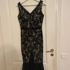 Svart spetsklänning från Trend - Elegant svart spetsklänning från Trend med v-ringning och vacker spetsdetalj. Klänningen har en figurnära passform och är tillverkad i polyester. Perfekt för en speciell kväll!