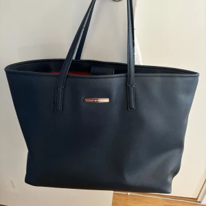 Svart axelväska från Tommy Hilfiger - Snygg svart axelväska från Tommy Hilfiger med stilren design. Har använts sparsamt men har lite defekt på banden, men inget som förstör. Kan skicka bild om önskas🩷🩷