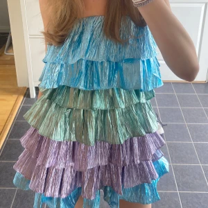 Flerfärgad klänning - Säljer en färgglad  klänning med volanger i blå, grön och lila, den är använd 2 gånger så är som ny, inga defekter. Den har band som man kan vika in (Se bild 4)❣️❣️Dom 2 första bilderna är lånade bilder men bild 3 och 4 är mina egna❣️