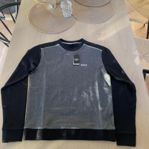 Grå och svart tröja från BOSS - Snygg grå och svart tröja från BOSS med rund hals och långa ärmar. Perfekt för en avslappnad stil. Diskret BOSS-logga på bröstet och kontrasterande vita detaljer vid axlarna. 🌟Rating ⭐️⭐️⭐️⭐️⭐️ 📏Size S