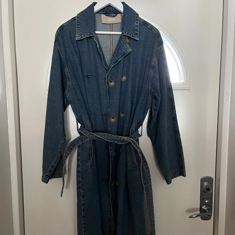 Snygg jeanskappa från JXX med knappar och bälte i midjan. Den har en klassisk krage och långa ärmar. Perfekt för en avslappnad stil med en touch av denim.. Takit.