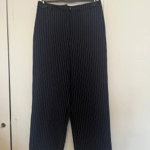 Randiga kostymbyxor från BikBok - Snygga mörkblå kostymbyxor från BikBok med vita ränder. Byxorna har en klassisk design med knappar och dragkedja framtill. Passar också på 42. Perfekta för en stilren look. Aldrig använda ❣️