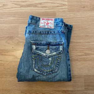 True Religion Jeans Bootcut Flare  - !skicka bud för snabb affär! Fina true religion jeans, model med ”pacthes” samt distressing. Lagring på ena benet längst ner. Bra skick annars och i storlek26. Mått:                                                             Midja 34 cm  Ytterben 102 cm  Innerben 80 cm  Ben öppning 22 cm