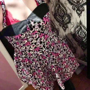 Klänning från Hell Bunny - Säljer en unik klänning från Hell Bunny med ett coolt mönster i svart, rosa och vitt. Klänningen har knappar framtill och ett lekfullt tryck med dödskallar och rosetter. Perfekt för dig som vill sticka ut!