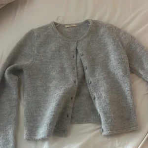 Grå kofta från Gina Tricot - Mysig grå kofta från Gina Tricot i premiumkvalitet. Den har långa ärmar och knappar framtill. Enkel och stilren design som passar till det mesta.