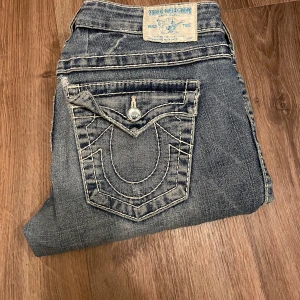 True Religion jeans - Säljer ett par snygga blå jeans från True Religion med coola detaljer på bakfickorna. De är omsydda till bootcut och även sydda på lite här å där💕