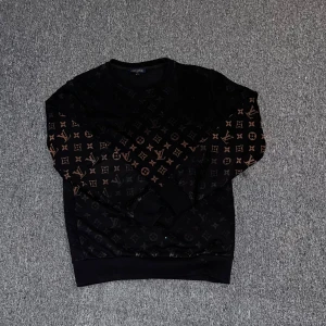 Svart tröja från Louis Vuitton - Säljer en svart tröja från Louis Vuitton med det ikoniska monogrammönstret i brunt. Tröjan har långa ärmar och en rund halsringning. Perfekt för dig som vill ha en stilren och lyxig look.