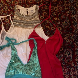 Fyra olika toppar - Säljer fyra snygga toppar i olika stilar. En vit halterneck med spetsdetaljer, en vit ärmlös blus med broderad krage, en röd oneshoulder topp och en turkos paljettlinne. Perfekta för olika tillfällen och stilar!