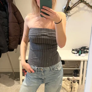 Tub/korsett topp - Snygg randig tubtopp i grått och vitt. Den sitter figurnära, och är i kostym-material. Finns dragkedjor på baksidan samt sidorna. Använd fåtal gånger. Frakt ingår! 