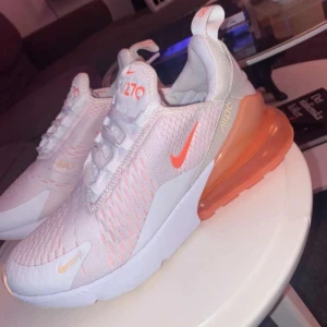 Nike Air Max 270 i vitt och orange - Säljer ett par Nike Air Max 270 i vitt med orange detaljer. Använda fåtal gånger och är i väldigt bra skick. Storlek 38,5. Men passar 38. Nypris 1900