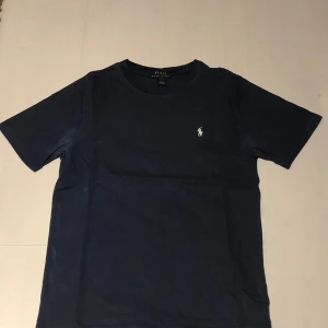 Blå t-shirt från Ralph Lauren - Säljer en klassisk blå t-shirt från Ralph Lauren med det ikoniska broderade logotypen på bröstet. Perfekt för en stilren och avslappnad look. Priset är inte hugget i sten.