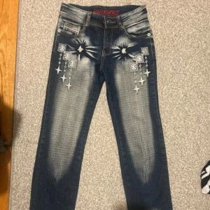 Blå jeans med broderade detaljer - Snygga blå jeans med unika broderade stjärndetaljer och blekta effekter. Jeansen har en klassisk femficksdesign och en normal passform. Perfekta för att ge din outfit en cool touch.