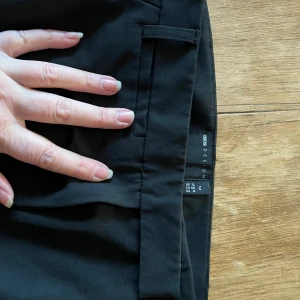 Svarta kostymbyxor från ASOS - Snygga svarta kostymbyxor från ASOS med en klassisk design. Byxorna har en knapp och dragkedja framtill samt hällor för bälte. Perfekta för en stilren look.Extra långa ben