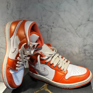 Nike Air Jordans i orange och vit - Snygga Nike Air Jordans i en fräsch kombination av orange och vit. Skorna har klassisk snörning och en ikonisk design med Nike-loggan på sidan. Perfekta för dig som vill sticka ut med stil.