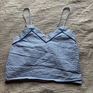 Blå- och vitrandig linnetopp från Hunkemöller - Säljer en söt blå- och vitrandig linnetopp från Hunkemöller. Toppen har smala axelband och en v-ringad design. Perfekt för varma sommardagar. 💙Passar XXS-S!