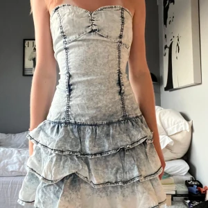 Jeansklänning - Snygg axelbandslös klänning i jeanstyg! Den har en dragkedja på sidan och volanger nedtill.