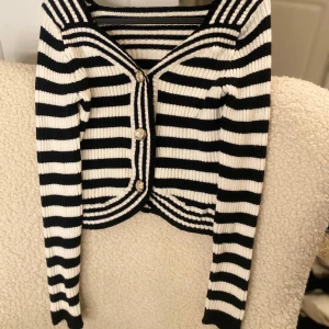 Svartvit randig kofta med knappar - Snygg svartvit randig kofta med dekorativa knappar framtill. Den har långa ärmar och en ribbad struktur som ger en stilren look. Perfekt för att lägga till en touch av elegans till din outfit.