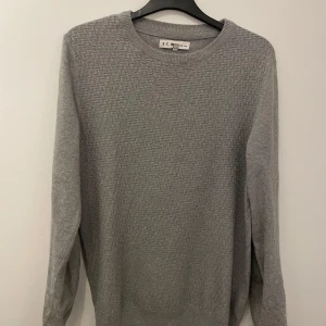 Grå tröja från S.C.W - Säljer en stilren grå tröja från S.C.W i storlek S. Tröjan har ett diskret mönster och är långärmad med ribbade kanter vid hals, ärmslut och nederkant. Perfekt för en avslappnad och bekväm stil. Skriv om ni har funderingar och priset är inte hugget i sten!