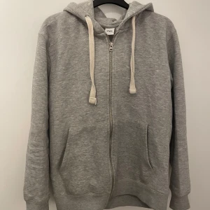 Grå hoodie med dragkedja - Säljer en stilren grå hoodie från Zara med dragkedja och justerbar huva. Tröjan har långa ärmar och praktiska fickor framtill. Perfekt för en avslappnad look. Skriv om ni har funderingar och priset är inte hugget i sten!