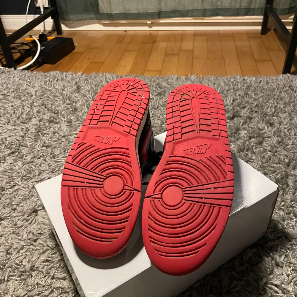 Snygga Nike Air Jordan 1 Low sneakers i svart och röd färg. Skorna har en klassisk design med snörning och en kontrasterande röd sula. Perfekta för dig som vill ha en stilren och sportig look.. Kengät.