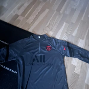 Grå psg set - Snyggt grått psg set från Nike med långärmad tröja och byxor. Tröjan har en halv dragkedja och röd logga på bröstet. Byxorna har en röd Nike-logga och elastisk midja för komfort. Perfekt för träning eller avslappning. 