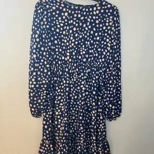 Snygg klänning med blå bas och beige prickigt mönster. Den har långa ärmar och en elastisk midja för en bekväm passform. Perfekt för en stilren look. Har endast haft på mig ett par gånger så i ett super skick.