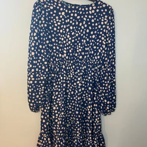 Mönstrad klänning i blått och beige - Snygg klänning med blå bas och beige prickigt mönster. Den har långa ärmar och en elastisk midja för en bekväm passform. Perfekt för en stilren look. Har endast haft på mig ett par gånger så i ett super skick.