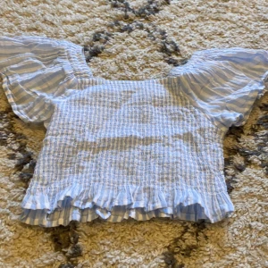 Blå- och vitrandig topp från Kappahl - Söt blå- och vitrandig topp från Kappahl med puffiga kortärmar och volangdetaljer i nederkant. Storlek 134/140💗