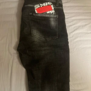 Svarta jeans från Dsquared2  - Snygga svarta jeans från Dsquared2 med coola slitningar och färgstänk. De har en klassisk femficksdesign och en knappgylf. Perfekta för en trendig look.