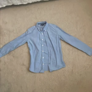 Ljusblå skjorta från Tommy Hilfiger - Säljer en stilren ljusblå skjorta från Tommy Hilfiger. Den har långa ärmar och klassiska knappar framtill. Perfekt för både vardag och fest! Skjortan är i bra skick och redo för en ny ägare.