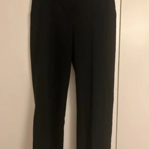 Kostymbyxor NAKD - Svarta långa kostymbyxor med en slits och pressveck framtill från NAKD. Storlek 38, väldigt bra skick!