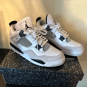 Nike Air Jordans i vit och svart - Säljer ett par snygga Nike Air Jordans military black i vit och svart. Skorna har en klassisk design med snörning och det ikoniska Jumpman-logotypen på tungan och hälen. De är i nyskick och kommer i originalkartong. Perfekta för både vardag och fest!