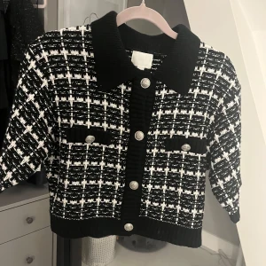Svart och vit rutig kofta - Säljer en snygg svart och vit rutig kofta med korta ärmar och stiliga knappar framtill. Den har en klassisk krage och två dekorativa fickor. Perfekt för både vardag och fest! Slutsåld på hemsidan 💕