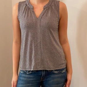 Mönstrad ärmlös topp - Snygg och bekväm ärmlös topp från H&M med ett diskret mönster i svart och vitt. Toppen har en v-ringad hals och är perfekt för både vardag och fest. Materialet är mjukt och följsamt, vilket gör den skön att bära hela dagen.