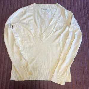 Vit v-ringad tröja från Gina Tricot - Säljer en stilren vit tröja från Gina Tricot i storlek XS . Den har en snygg v-ringning och ett diskret broderat emblem på bröstet. Tröjan är långärmad och har ribbade kanter vid ärmslut och nederkant. Perfekt för både vardag och fest!