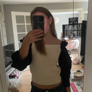 beige stickad offshoulder topp med puff ärm - Säljer en superfin vit stickad offshoulder topp. Den är croppad och har en snygg passform som passar perfekt till både vardag och fest. Toppen är använd fåtal gånger ger en stilren look med sina långa svarta ärmar som kontrasterar snyggt mot det vita. Något liten i storleken!