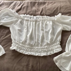 Vit offshoulder blus - Säljer en superfin vit offshoulder blus med volangdetaljer. Den har långa ärmar och en elastisk midja som ger en snygg passform. Perfekt för sommarens fester eller en dag på stan. 🕊️