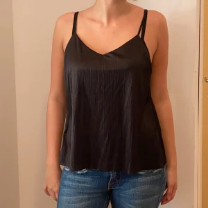 Svart linnetopp från Amisu - Snygg svart linnetopp från Amisu i storlek S. Toppen har tunna axelband och ett lätt glansigt material som ger en elegant touch. Perfekt för både vardag och festliga tillfällen. Passar bra till jeans eller kjol för en stilren look.