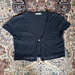 Svart glittrig kort croppad kofta - Jättesöt croppad svart silvrig kofta med dekorativa hål i sig. Står storlek XL men faller jättefint på mig som har storlek 36/38 <33 inga defekter, säljer då jag har många liknande