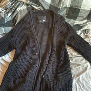 Svart stickad kofta från 157 - Mysig svart stickad kofta från 157 i storlek M. Perfekt för kyliga dagar med sina långa ärmar och knappar framtill. Den har praktiska fickor. Ett måste för höst- och vintergarderoben! 🍂