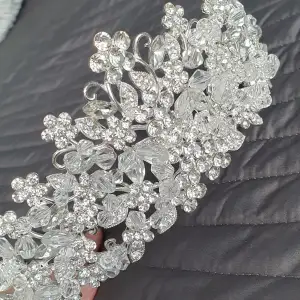 Säljer ett fantastiskt glittrigt diadem med vackra pärlor och detaljer. Perfekt för fest eller speciella tillfällen. Diademet har en elegant design med blommönster och är i en skimrande silverfärg. Det är både stilrent och iögonfallande, vilket gör det till ett måste för att komplettera din look.