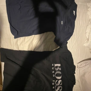 Svart och mörkblå t-shirt från Hugo Boss - Två stilrena t-shirts från Hugo Boss i svart och mörkblått. Båda har korta ärmar och klassisk passform. Den svarta t-shirten har ett stort BOSS-tryck på framsidan medan den mörkblå har en diskret logga på bröstet. Perfekta för vardagsbruk eller en avslappnad kväll. Hugo boss: 150 kr boss 300kr