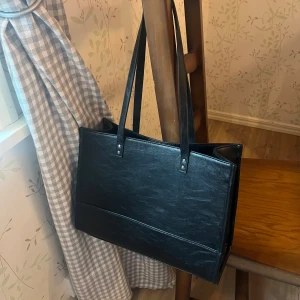 Läder tote väska - Snygg och stilren svart axelväska i skinn. Perfekt för både vardag och jobb med gott om plats för alla dina saker. Väskan har långa remmar för bekväm bärning och en enkel design som passar till allt. Ett måste för den som vill ha en praktisk men ändå chic väska!