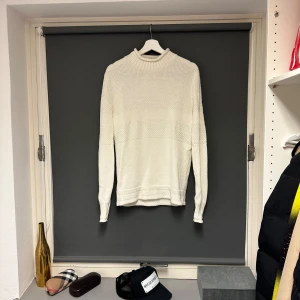 Vit stickad tröja från Selected Homme - Säljer en stilren vit stickad tröja från Selected Homme. Den har en klassisk design med ribbad krage och långa ärmar. Perfekt för både höst och vinter, och passar till många olika outfits. Tröjan är i bra skick och redo för en ny ägare!