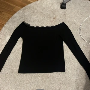 Svart offshoulder topp från Bik Bok - Säljer en snygg svart offshoulder topp från Bik Bok i storlek S. Toppen har långa ärmar och en fin spetsdetalj längs kanten. Perfekt för både vardag och fest! 🖤